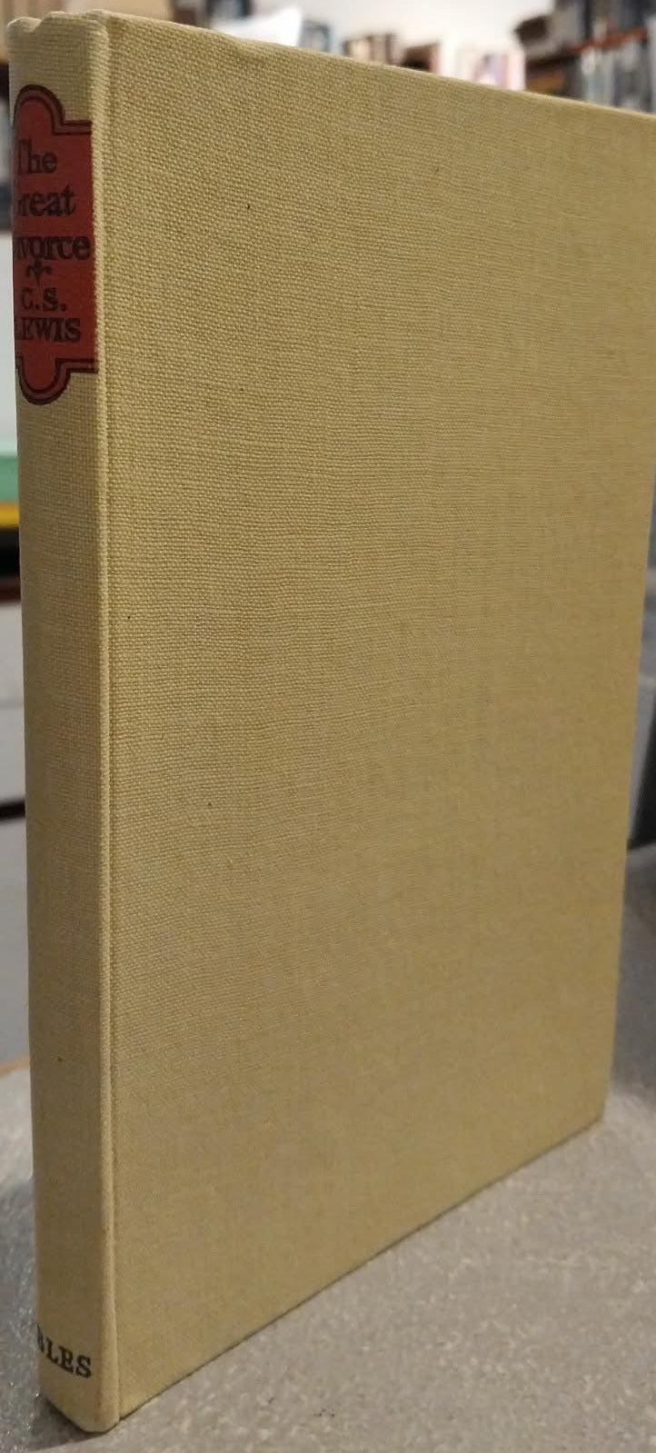 A vintage hardcover book with a textured light beige cloth cover and a red spine label, standing upright on a tabletop in an indoor setting.