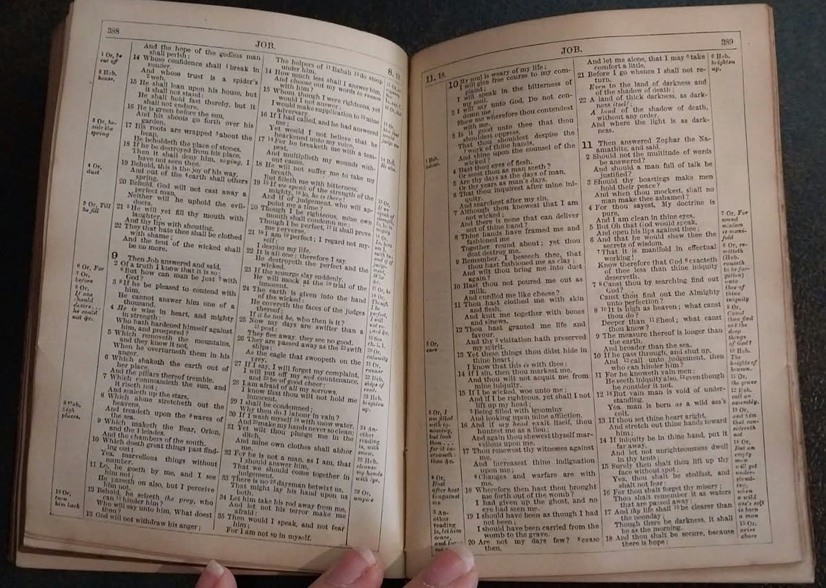 An open vintage dictionary or book with dense columns of printed text, held open by a hand against a dark textured background.