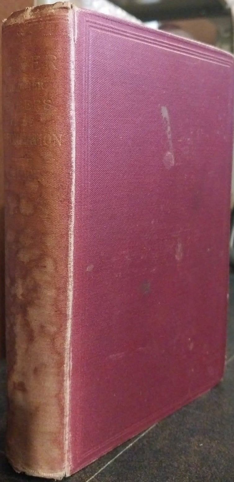 An antique hardcover book with a dusty rose pink front cover and a weathered brown spine, standing upright on a dark surface.