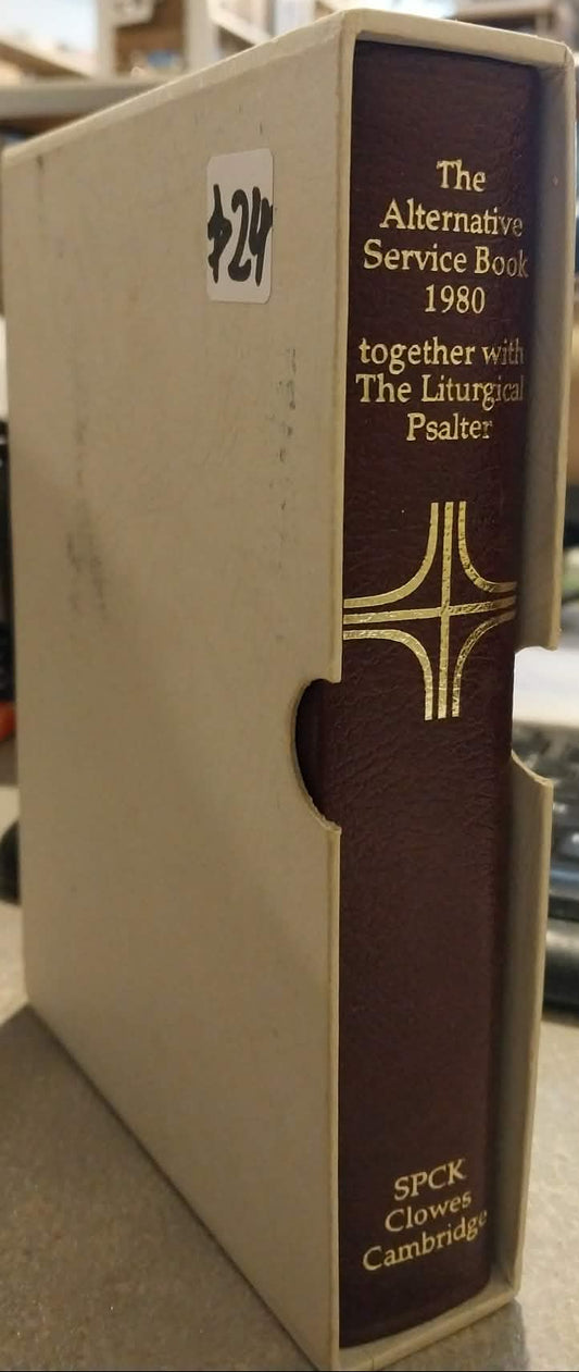 A boxed liturgical book set standing on a desk in a real indoor environment, with a keyboard and shelves visible in the background. The set includes a cream-colored outer box and a dark brown spine panel with gold text reading 'The Alternative Service Book 1980 together with The Liturgical Psalter' and 'SPCK Cloves Cambride.
