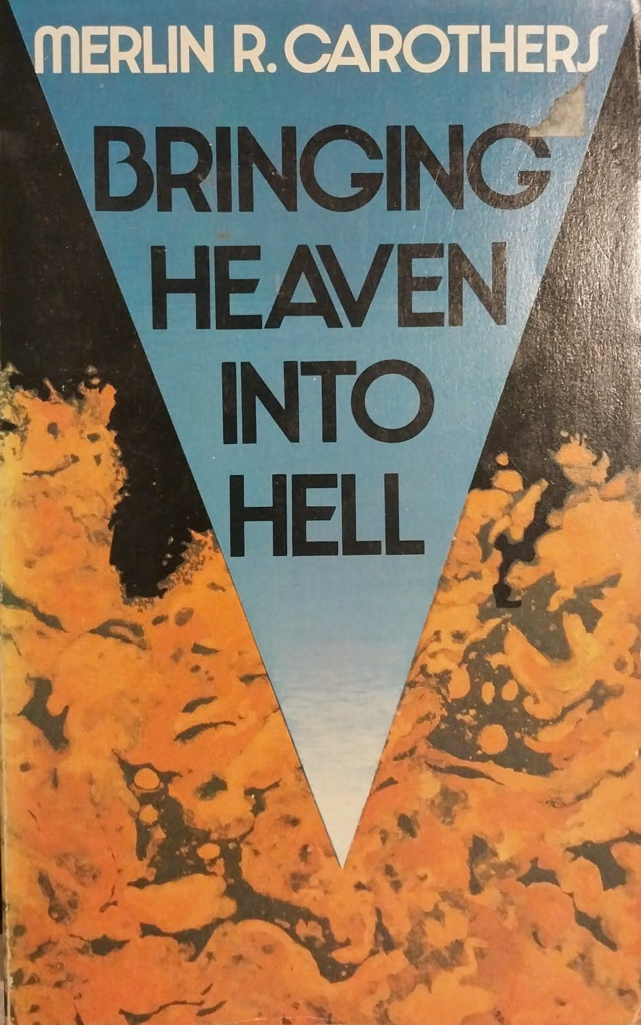 A vintage paperback book of Merlin R. Carothers' 'Bringing Heaven Into Hell' with a graphic cover featuring a blue inverted triangle over an orange and black marbled background, photographed on a textured gray surface.