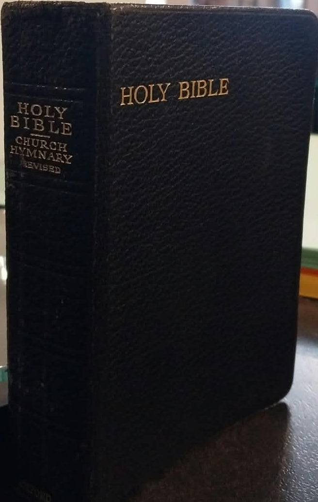 A black textured leather Holy Bible standing upright on a dark tabletop in a shop or library setting, with gold lettering on the front and spine.