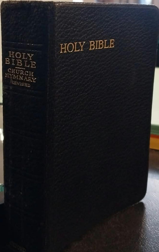 A black textured leather Holy Bible standing upright on a dark tabletop in a shop or library setting, with gold lettering on the front and spine.