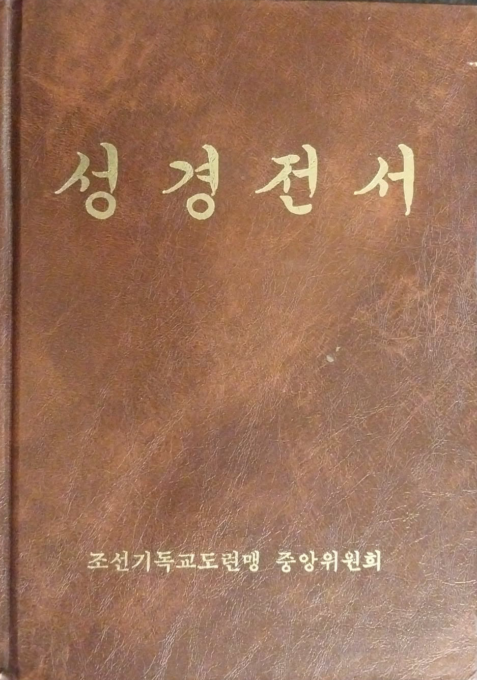 A brown leather-bound book with gold Korean text on the cover, photographed from above on a dark textured surface.