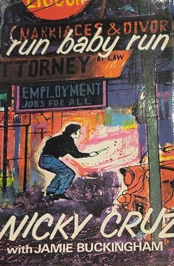 A vintage paperback book titled 'Run Baby Run' by Nicky Cruz with Jamie Buckingham, featuring a colorful illustrated cover with a woman and urban background elements.