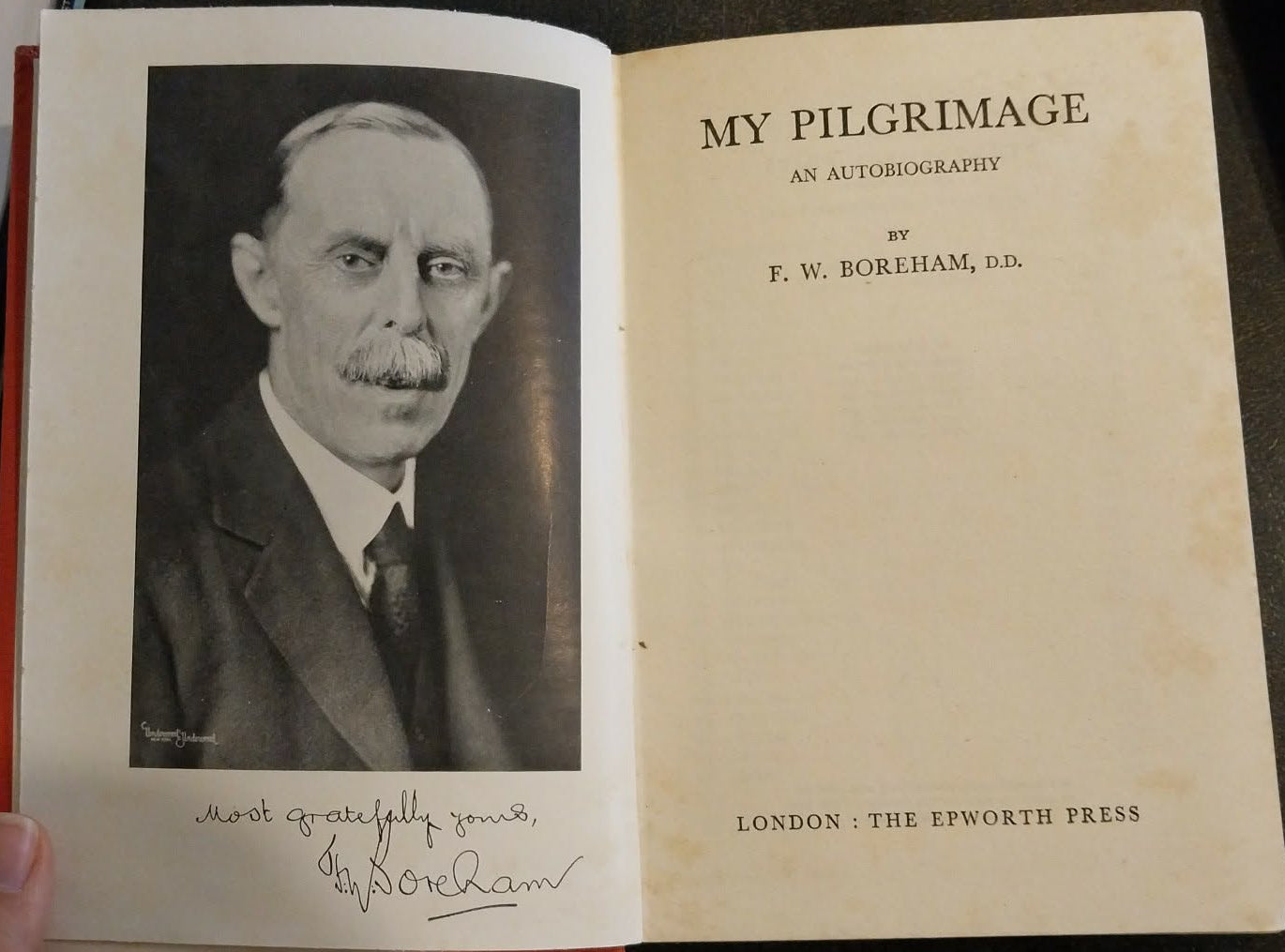 Book titled 'My Pilgrimage' with a portrait inside, held open by a hand.