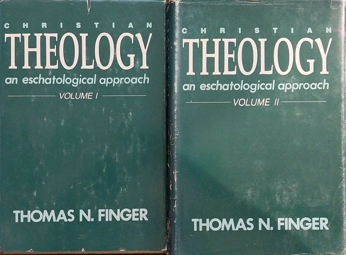 Two books titled 'Theology' by Thomas N. Finger on a wooden surface.