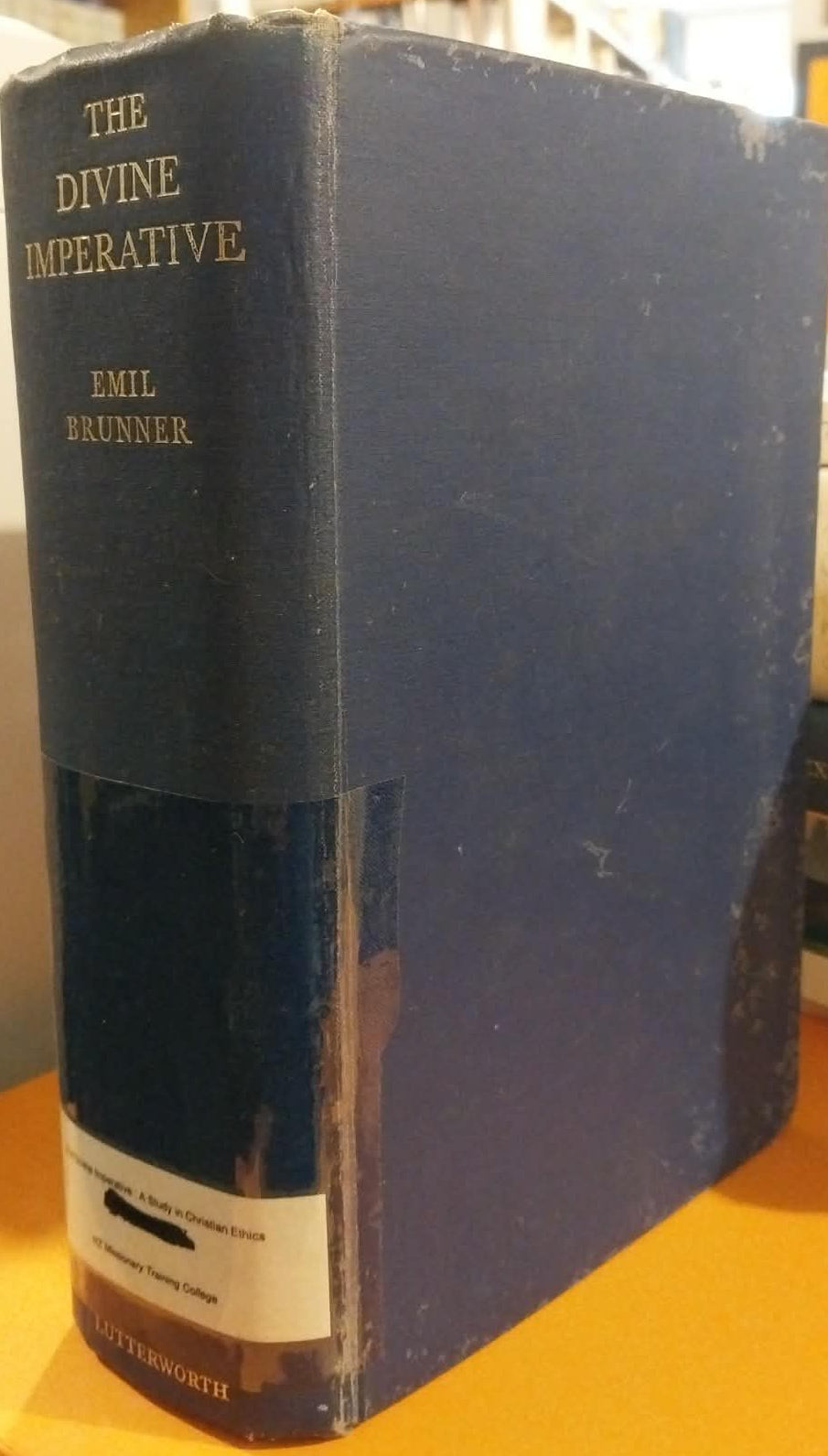 Vintage book titled 'The Divine Imperative' by Emil Brunner on a yellow surface.