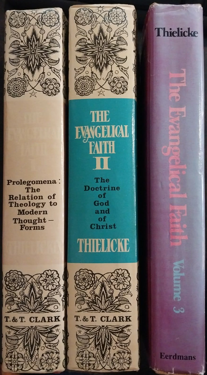 Three vintage theological books standing upright on a black keyboard. The left book is cream with black floral border and gold text; the middle book has a turquoise center panel with gold text and cream borders; the right book is purple with gold text.