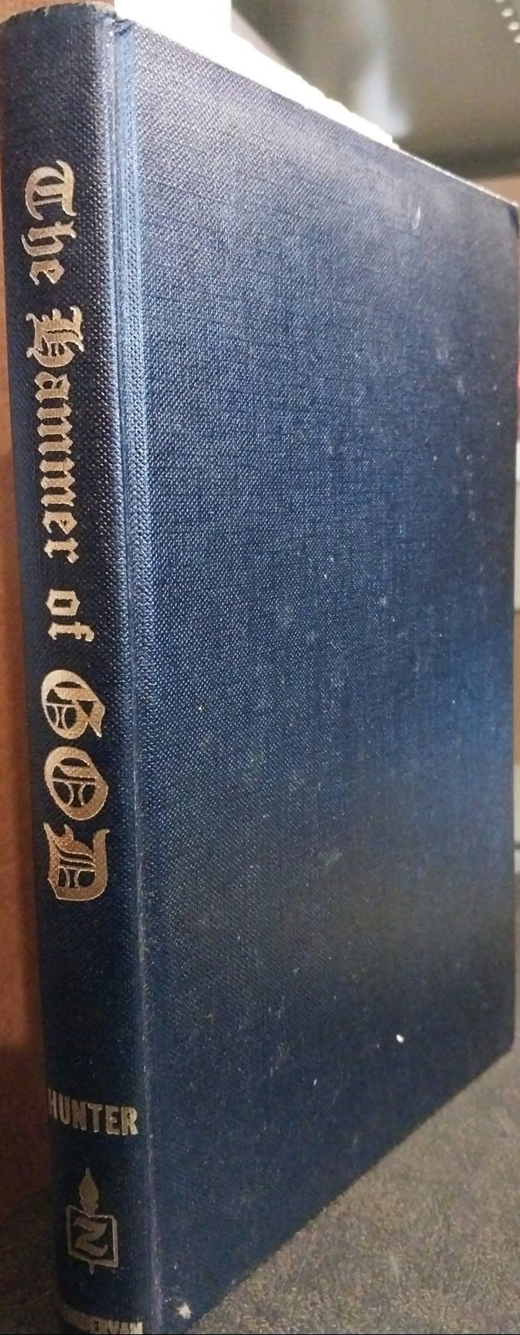 A vintage hardcover book titled 'The Hammer of God' by Hunter, featuring a dark blue textured cloth cover with gold lettering on the spine, photographed standing upright on a shelf.