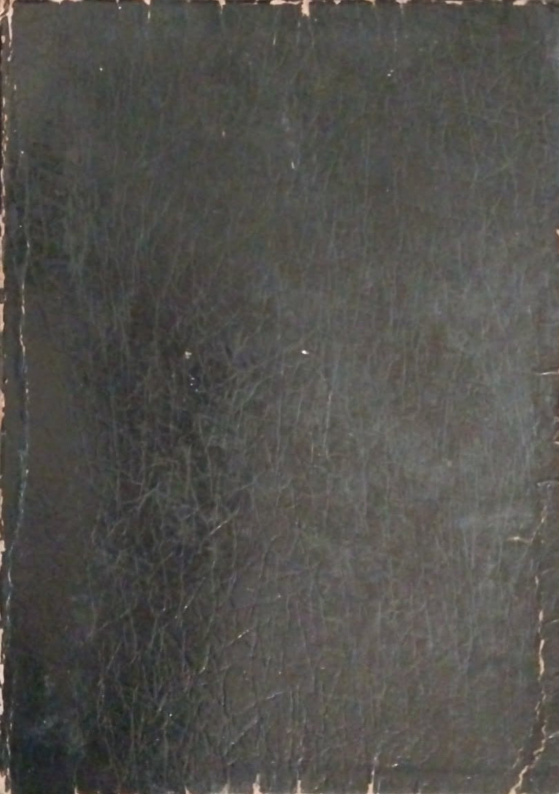 A black leather-bound book or journal lying flat on a dark tabletop, with visible worn edges and a textured cover.