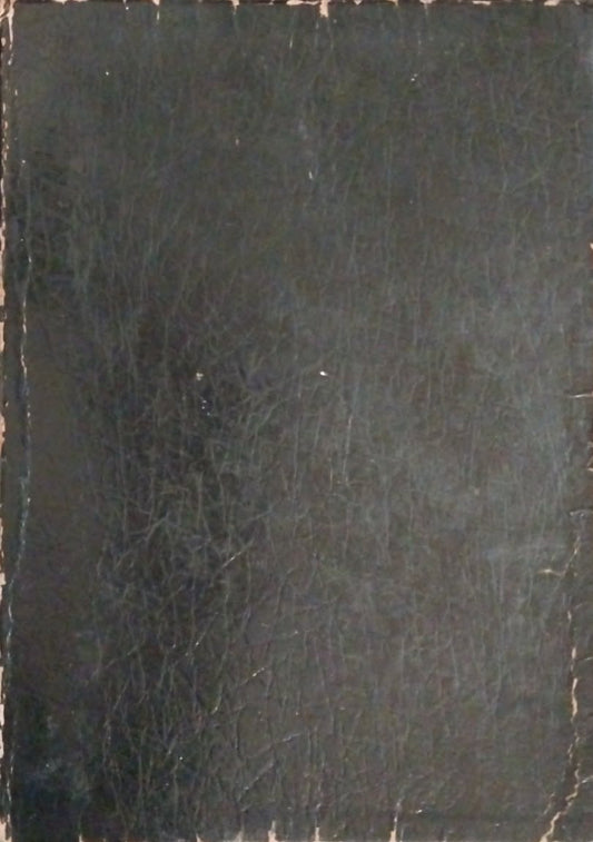 A black leather-bound book or journal lying flat on a dark tabletop, with visible worn edges and a textured cover.