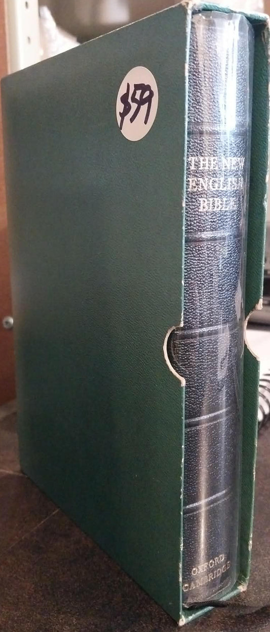 A green hardcover Bible, The New English Bible, standing upright on a dark tabletop. The spine is visible, showing the title in white text, and there is a white circular sticker with the number 359 on the front cover.