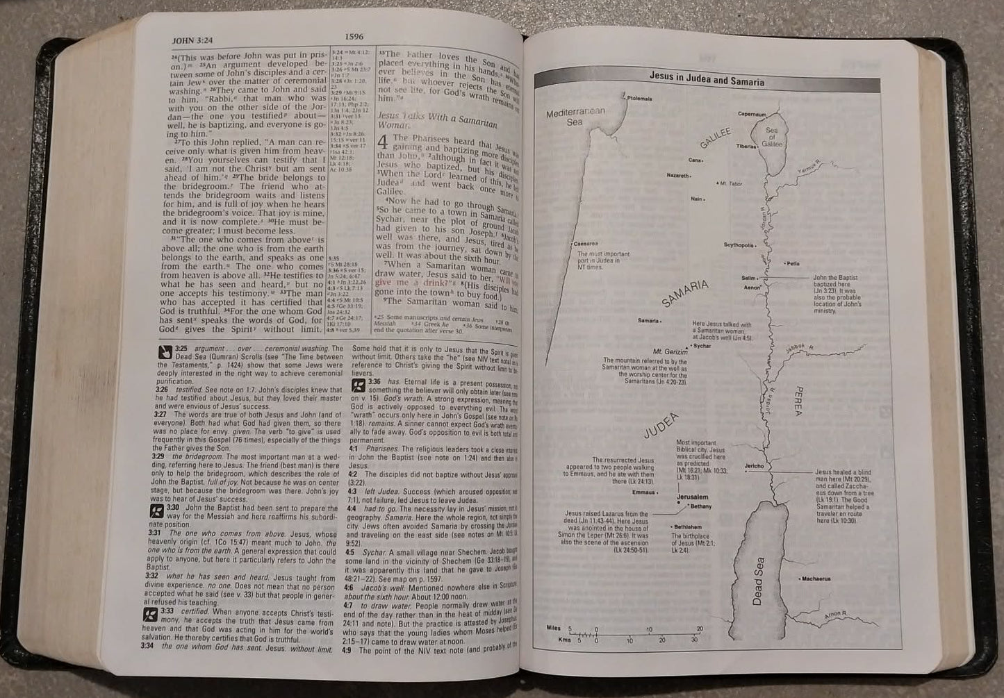 An open Bible with printed text on the left page and a map or diagram on the right page, resting on a gray surface.