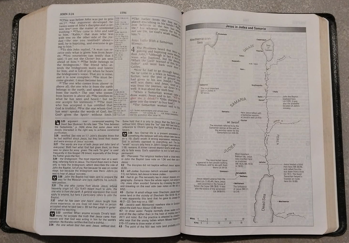 An open Bible with printed text on the left page and a map or diagram on the right page, resting on a gray surface.