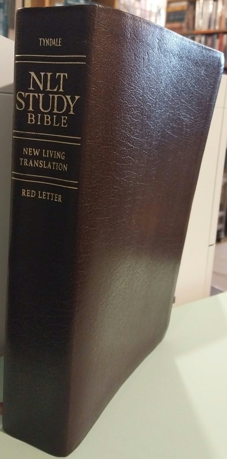A dark brown leather-bound NLT Study Bible standing upright on a light-colored surface, with a blurred bookshop background.