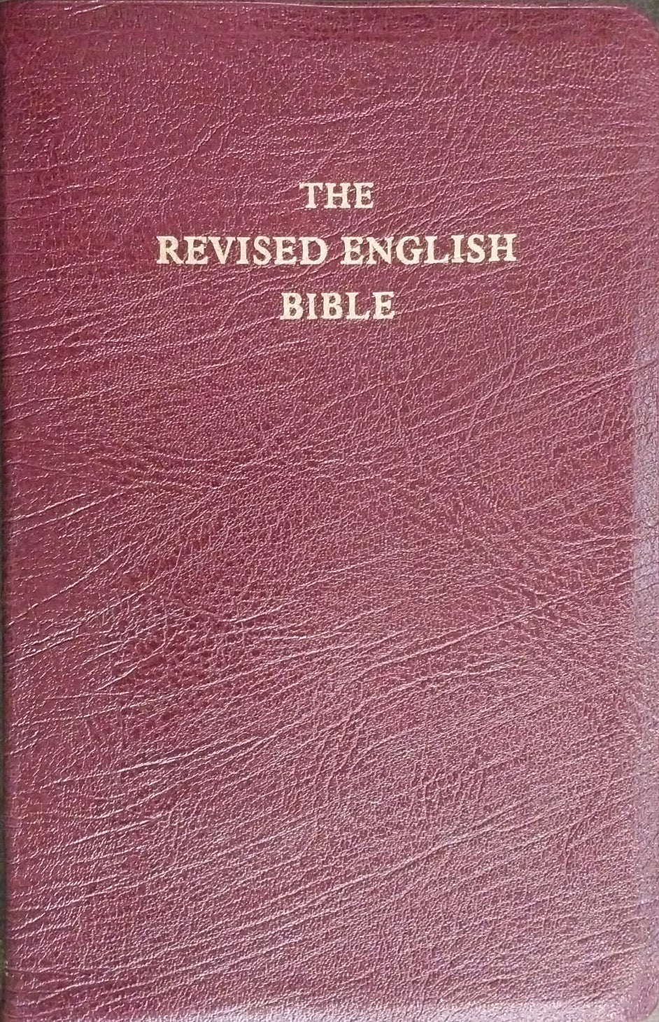 The Revised English Bible in a textured burgundy leather-bound cover with gold lettering, photographed flat on a dark textured surface.