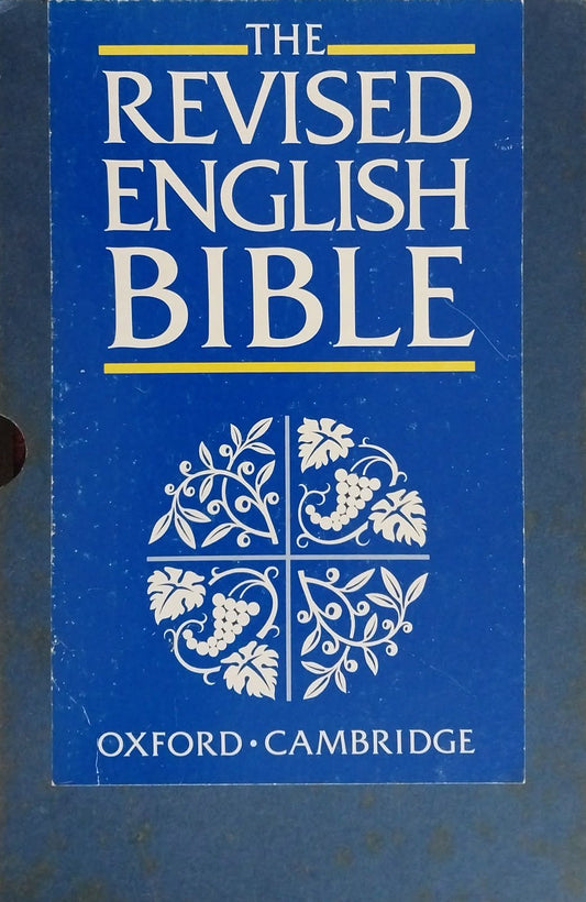 The Revised English Bible book by Oxford-Cambridge, featuring a blue cover with white text and decorative floral motifs, photographed on a dark brown surface.