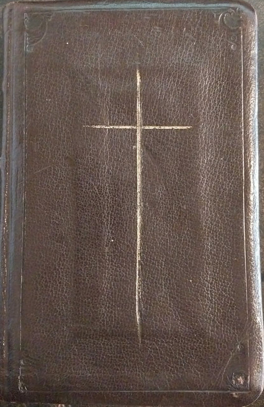 Brown leather-bound book with a cross on the cover, placed on a green surface.