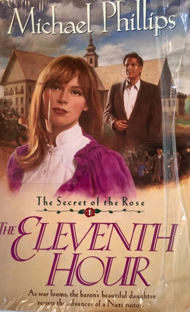 A paperback book of Michael Phillips' 'The Eleventh Hour: The Secret of the Rose' lying on a light-colored fabric surface. The book cover features a romantic illustration of a woman in a purple dress and a man in a suit against a village background.