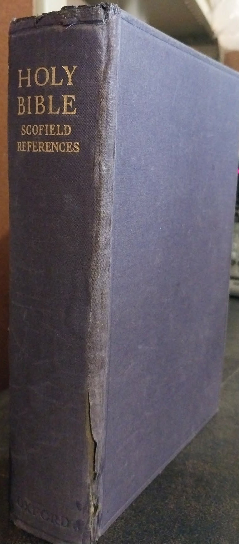 A vintage Holy Bible Scofield References book with a dark purple cloth binding and gold lettering on the spine, standing on a dark surface in an indoor setting.